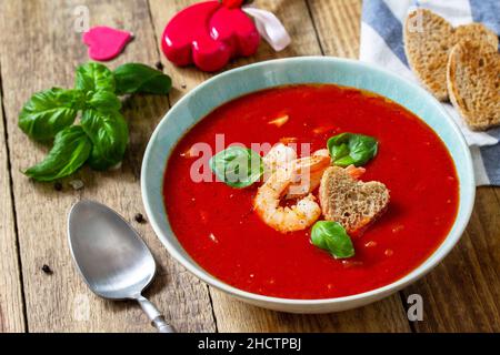 Soupe de Saint-Valentin maison, repas de fête.Soupe de tomates, purée de gazpacho avec tomates, fruits de mer servis sur une table rustique en bois. Banque D'Images