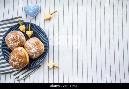 Bonne Hanoukkah.Un régal traditionnel de beignets avec David star et dreidel fait à partir de fromage et de bâtonnets de biscuit.Décoration coeur en tissu bleu.Copier l'espace. Banque D'Images