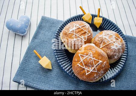 Bonne Hanoukkah.Un régal traditionnel de beignets avec David star et dreidel fait à partir de fromage et de bâtonnets de biscuit.Décoration coeur en tissu bleu.Copier l'espace. Banque D'Images