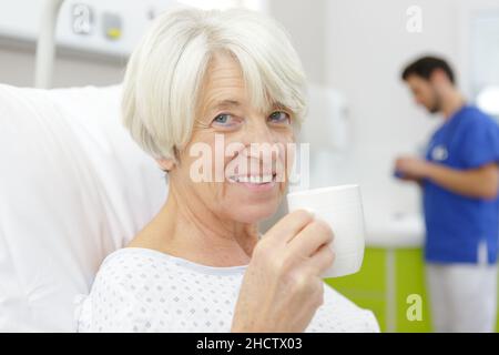 une femme âgée buvant du café sur le lit d'hôpital Banque D'Images