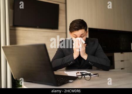 Un jeune homme malade au travail est devenu allergique à la grippe, aux éternuements et au jeûne, essuyant un nez qui coule avec une serviette en papier, un gars allergique a attrapé un rhume au travail Banque D'Images