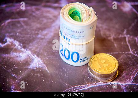 Rouler les billets israéliens Shekel ils près des jetons de crypto-monnaie bitcoins pièces de bits, vu d'en haut, sur un vieux panneau de marbre.Mise au point sélective. Avec espace pour le placement du texte.Photo de haute qualité Banque D'Images