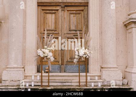 Des bouquets de fleurs se trouvent sur des plinthes dorées devant une porte en bois de l'église Banque D'Images