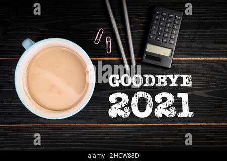 Au revoir 2021.Tasse à café, calculatrice et crayons sur fond de bois noir. Banque D'Images