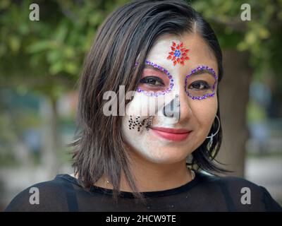 Jeune femme mexicaine de race blanche avec maquillage traditionnel peint de visage regarde le spectateur pendant le festival de jour des morts (Dia de los Muertos). Banque D'Images