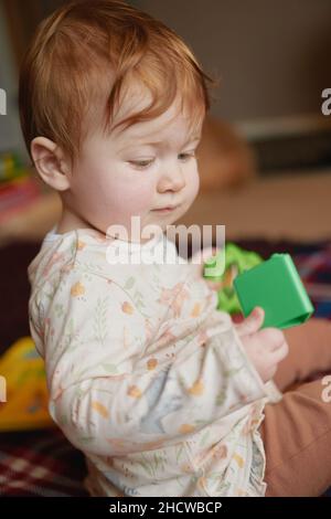 Une petite fille de dix mois à tête rouge avec des jouets Banque D'Images