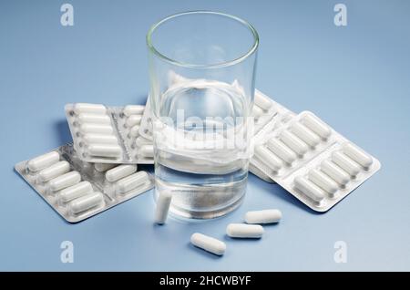 Verre d'eau et capsules de médicaments emballés dans des cloques sur une table bleue Banque D'Images
