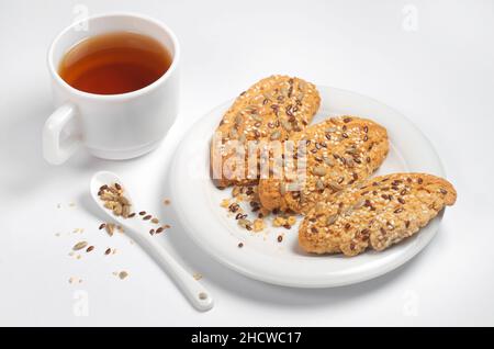 Biscuits aux graines de tournesol et au sésame dans une assiette et une tasse de thé sur fond blanc Banque D'Images