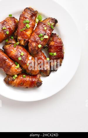 Ailes de poulet grillées enveloppées de bacon sur une assiette sur fond de pierre blanche avec espace de copie.Vue de dessus, plan d'appartement Banque D'Images