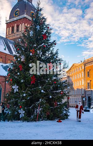 Le Père Noël marchant à côté de l'immense arbre de Noël à Riga, en Lettonie. Banque D'Images