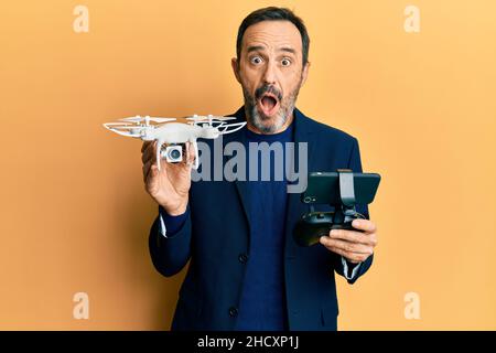 Homme hispanique d'âge moyen utilisant un drone peur et choqué avec la surprise et l'expression stupéfaite, la peur et le visage excité. Banque D'Images