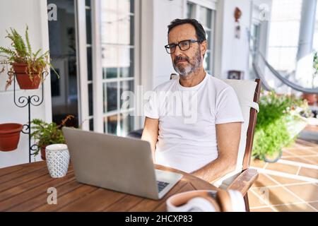 Homme d'âge moyen utilisant un ordinateur portable à la maison regardant somnolent et fatigué, épuisé pour la fatigue et la gueule de bois, les yeux paresseux le matin. Banque D'Images