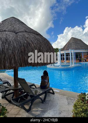 Femme bronzée assise près de la piscine sans personne.Belle piscine extérieure entourée de palmiers. Banque D'Images