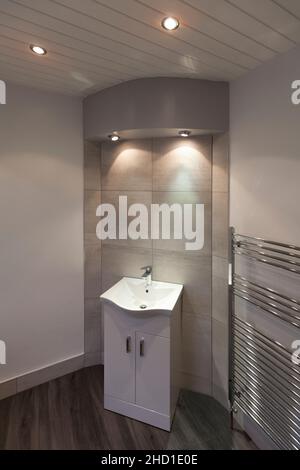 Salle de bains moderne avec meuble-lavabo, grands carreaux blancs Barrington, sol en vinyle LVT, murs gris et blancs, grand porte-serviettes, spots Banque D'Images