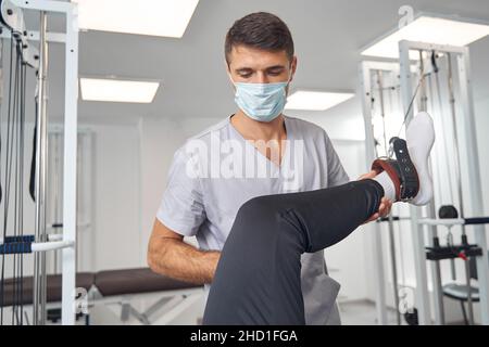 Kinésiologue caucasien concentré étirant les muscles des jambes du patient Banque D'Images