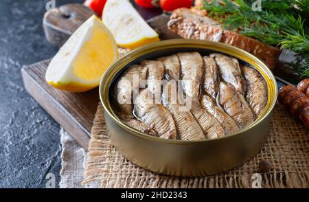 Les poissons de mer en conserve de la Baltique se sont enfumés dans une boîte de conserve sur fond noir.Ingrédients pour le smorrebrod. Banque D'Images