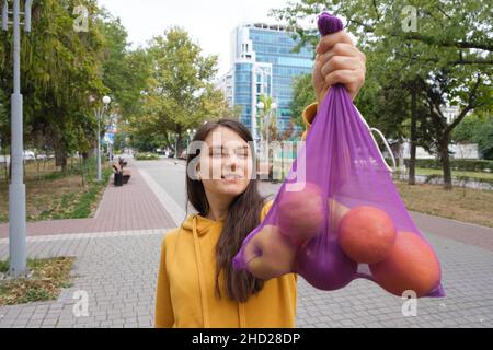 La femme montre un sac en tissu violet transparent avec des fruits. Banque D'Images