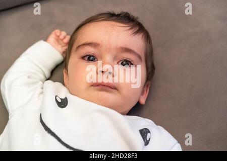 Bébé pleure avec la douleur de ses premières dents, allongé sur le canapé à la maison Banque D'Images