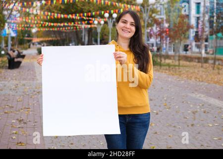 Une femme brune sourit et tient une feuille blanche vide pour l'inscription et le texte Banque D'Images