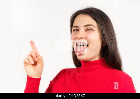 Une femme en rouge avec des pilules sur sa langue pointe son doigt à un endroit pour le texte Banque D'Images