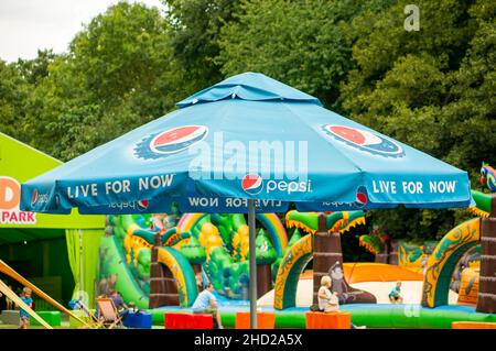 Grand parasol avec logo Pepsi contre un terrain de jeu par une journée ensoleillée dans le parc Frajda, Pologne Banque D'Images