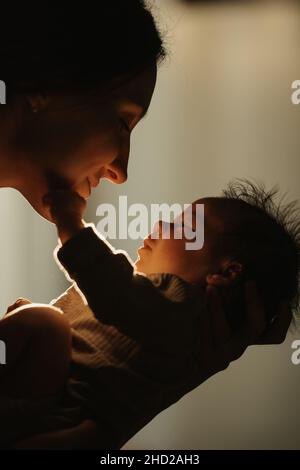 Gros plan de la mère heureuse qui tient le nouveau-né dans ses mains et l'embrasse.Le bébé souriant est en train de tendre la main à la maman Banque D'Images