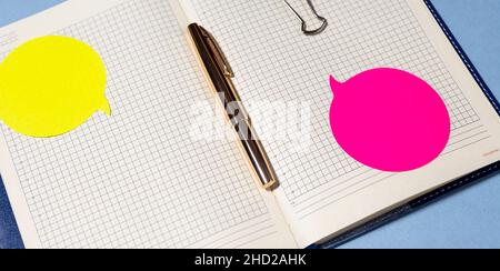 Ouvrez le bloc-notes contenant les fournitures de bureau.Le bloc-notes ouvert se trouve sur une table bleue avec un stylo doré et des autocollants lumineux Banque D'Images