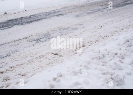 Chaussée enneigée glissante de la ville en hiver.Conditions météorologiques difficiles.Rue et trottoir sous des amas de neige.Circulation dangereuse. Banque D'Images