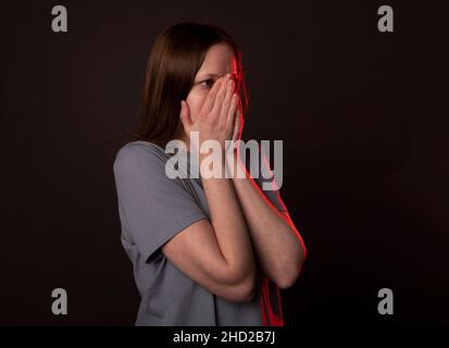 Jeune femme se cachant et couvrant son visage avec les mains, les paumes dans la peur ou la frustration. Banque D'Images