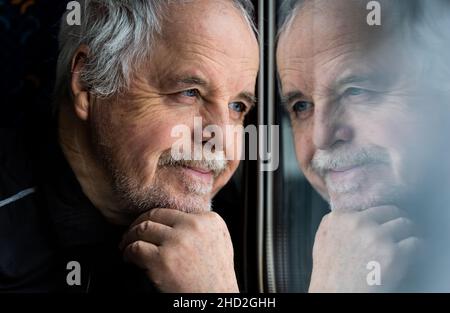 Homme senior regardant par la fenêtre, réflexion dans la fenêtre, smiling concept Banque D'Images