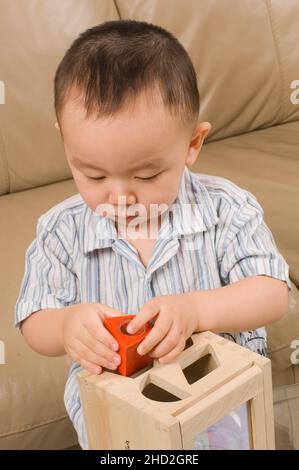 Famille américaine vietnamienne à la maison, jeune garçon jouant avec la forme géométrique trieur, en utilisant les deux mains pour tenir la forme Banque D'Images