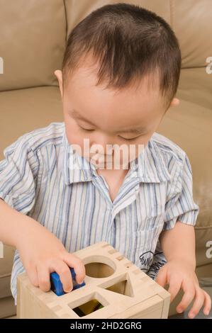 Famille américaine vietnamienne à la maison tout-petit garçon jouant avec la forme géométrique trieur, la forme qui s'adapte dans le trou Banque D'Images