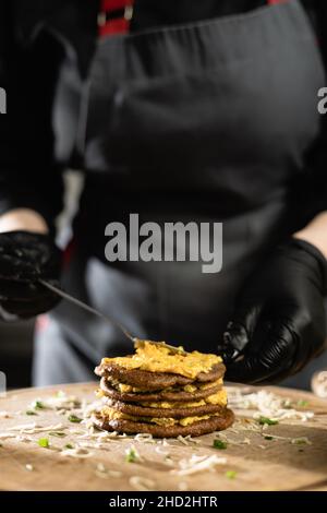 le chef prépare une tarte au foie dans la cuisine.Gros plan des mains de la femme en gants appliquez le remplissage entre les pancakes du foie. c Banque D'Images