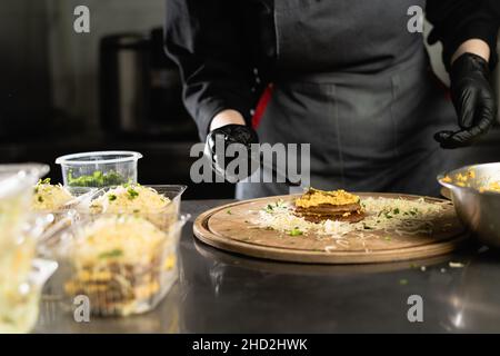 le chef prépare une tarte au foie dans la cuisine.Gros plan des mains de la femme en gants appliquez le remplissage entre les pancakes de foie. Banque D'Images