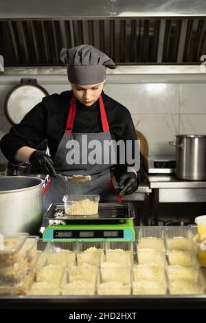 Livraison de la nourriture au restaurant. Le chef féminin en uniforme prépare la nourriture dans un restaurant et la prépare dans des plats jetables.Place des portions de riz dans Banque D'Images