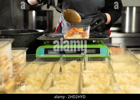 livraison de nourriture au restaurant.Gros plan de la main d'un chef ganté pesant un lot de riz sur une balance électronique.Petite entreprise.Plats à emporter. Banque D'Images