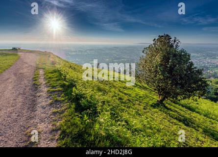 Une figure humaine lointaine, assise sur un banc de bois en observant en émerveillement le spectacle du soleil d'été qui s'élève au-dessus du paysage du Worcestershire, vu de Banque D'Images