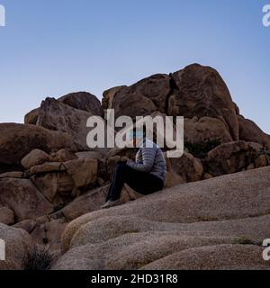 Le femelle Hiker est assis et attend Sunrise on Rocks dans le parc national de Joshua Tree Banque D'Images