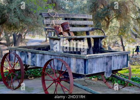 Vieux wagon de ferme en bois avec roues en fer rouge et banquette altérée sous les chênes dans un cadre rural extérieur. Banque D'Images