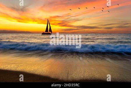 Un voilier navigue le long de l'océan avec un Flock of Birds survolant contre UN ciel coloré de coucher de soleil Banque D'Images