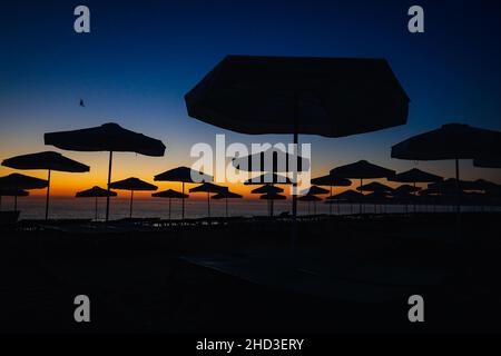 Silhouettes de parasols sur la plage juste avant le lever du soleil, le matin d'été calme et chaud à la mer Noire dans la station d'Obzor en Bulgarie. Banque D'Images