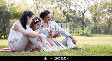 La famille asiatique utilise la tablette sur le tapis. Les filles apprennent à partir d'une tablette que les parents enseignent. Banque D'Images