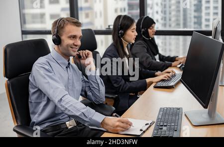 Homme de main caucasien et groupe de diverses équipes de télémarketing de service à la clientèle dans le centre d'appel.Employé du centre d'appels accompagné de l'équipe.Sourire Banque D'Images