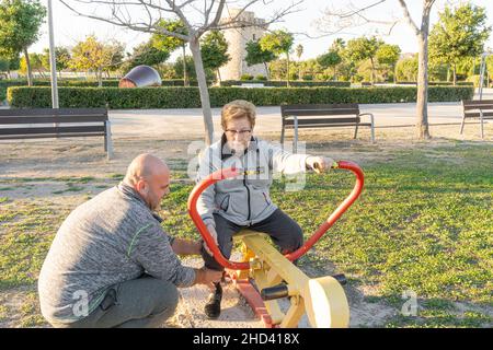 Un entraîneur masculin aide une femme plus âgée à faire de l'exercice sur la machine dans un parc bio-sain Banque D'Images