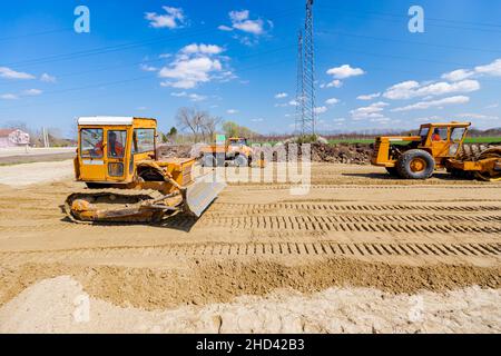 Le rouleau de route avec pointes, le bulldozer et le camion avec compacteur de vibrations à plaque monté sont compactés, nivelant le sable pour les fondations de la route sur le chantier Banque D'Images