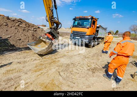 Une pelle tire un camion benne avec un cordon pour l'aider à sortir du sable sur le chantier. Banque D'Images