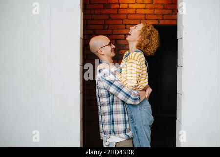 Un couple heureux amoureux à l'intérieur d'un appartement en construction.Il la soulève, elle rit, ils s'amusent. Banque D'Images