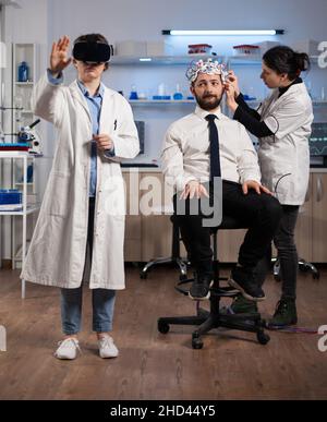 Chercheuse portant un casque de réalité virtuelle pendant une expérience de neurologie en laboratoire médical.Neurologue médecin Adujustiting eeg scanner surveillance activité cérébrale analyse système nerveux Banque D'Images