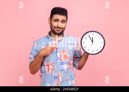 Regarde l'heure.Portrait de beau barbu gars dans le style décontracté chemise pointant grande horloge et regardant l'appareil photo, montrant des montres murales à Dépêche-toi.Studio d'intérieur isolé sur fond rose. Banque D'Images