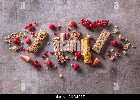 Diverses barres de muesli avec des raisins de Corinthe, des framboises et des fraises, ainsi que des céréales autour d'elles, vue du dessus. Banque D'Images